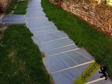 Senda de pizarra de superficie serrada con césped.