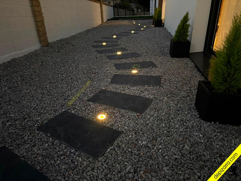 Senda de losas de pizarra con luces led empotradas en jardín de grava