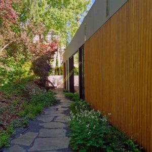 Camino de entrada de pizarra natural irregular junto a una vivienda moderna, rodeado de vegetación y jardín.