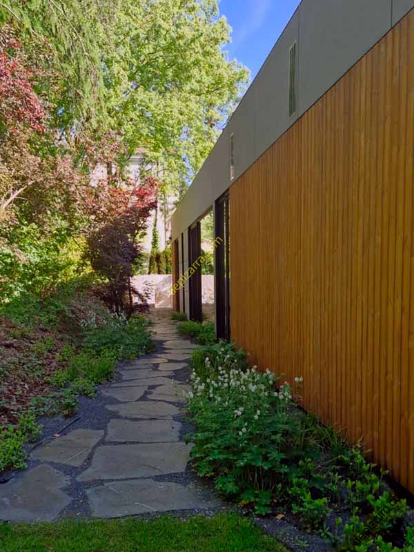 Camino de entrada de pizarra natural irregular junto a una vivienda moderna, rodeado de vegetación y jardín.